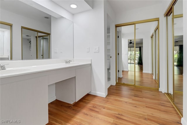 bathroom featuring toilet, a sink, wood finished floors, double vanity, and baseboards