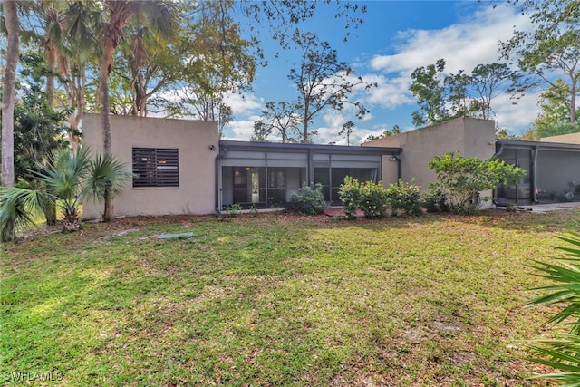 rear view of property with stucco siding, a yard, and a sunroom