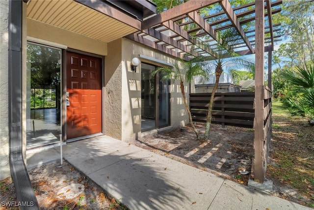 entrance to property with stucco siding, a pergola, and fence