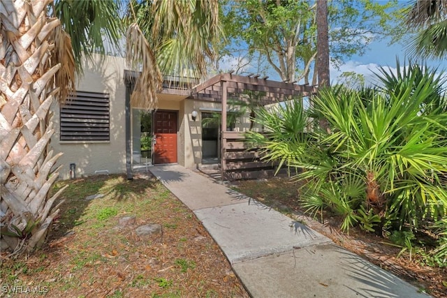 view of exterior entry featuring stucco siding and a pergola