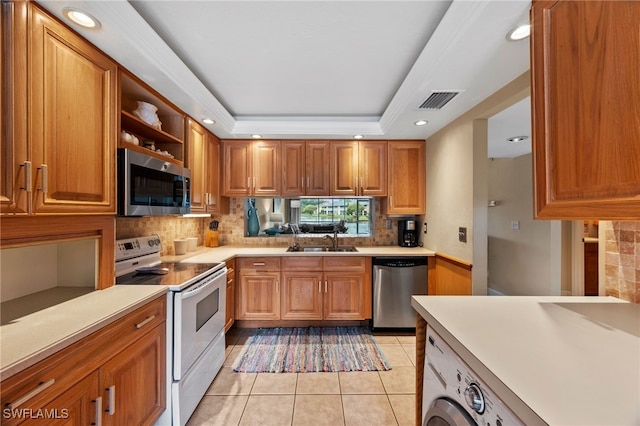 kitchen with appliances with stainless steel finishes, a tray ceiling, light countertops, and a sink