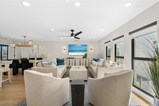 living room featuring light wood finished floors, recessed lighting, and ceiling fan with notable chandelier