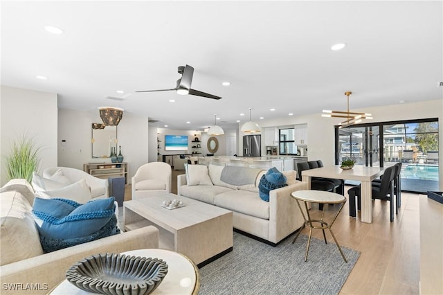 living room featuring ceiling fan with notable chandelier, recessed lighting, and light wood finished floors