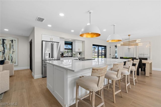 kitchen featuring visible vents, light wood-style flooring, a spacious island, white cabinetry, and high end refrigerator