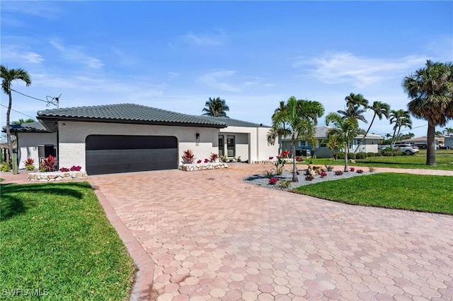 ranch-style house featuring an attached garage, a tile roof, decorative driveway, and a front yard