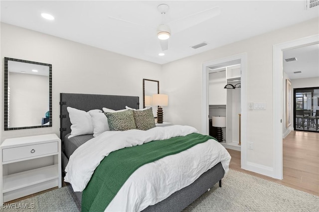 bedroom with visible vents, a walk in closet, baseboards, and wood finished floors