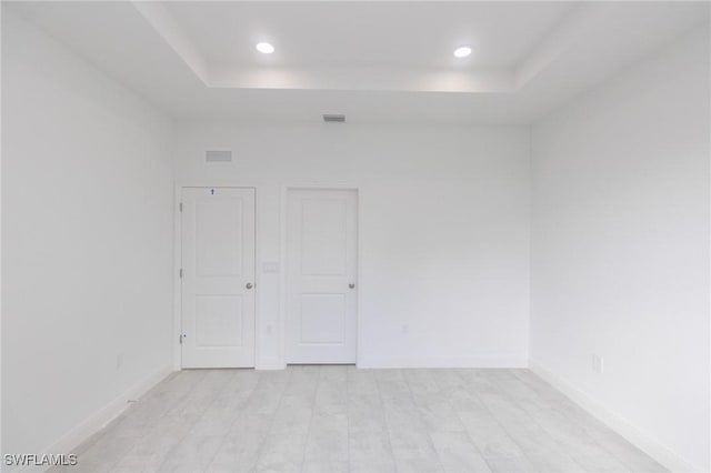 unfurnished room featuring a tray ceiling, light wood-type flooring, visible vents, and baseboards