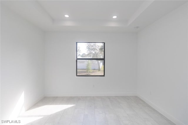 spare room featuring recessed lighting, a raised ceiling, and baseboards