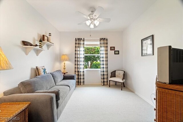 living area with baseboards, light carpet, and a ceiling fan