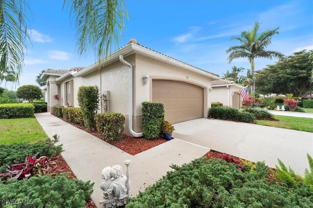 view of side of property with stucco siding, driveway, an attached garage, and a tiled roof