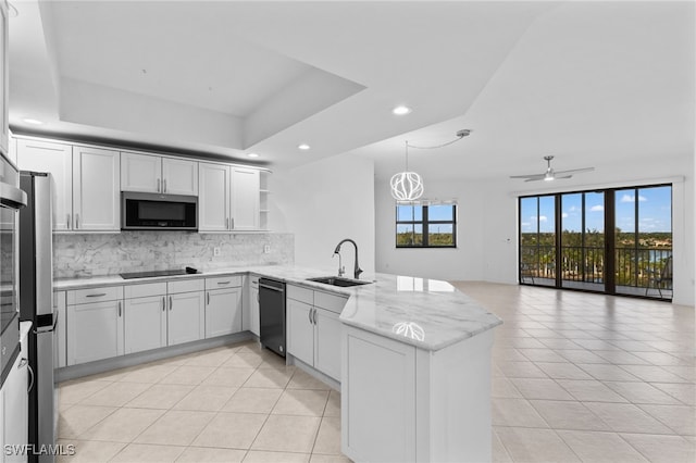 kitchen featuring backsplash, a tray ceiling, a peninsula, black appliances, and a sink