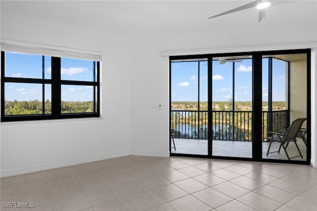 tiled empty room with a ceiling fan, a water view, and baseboards