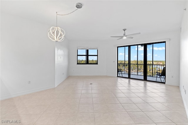 empty room with light tile patterned floors, baseboards, a healthy amount of sunlight, and ceiling fan with notable chandelier