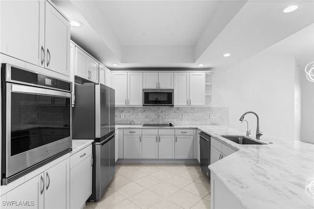 kitchen featuring decorative backsplash, black appliances, light stone countertops, and a sink