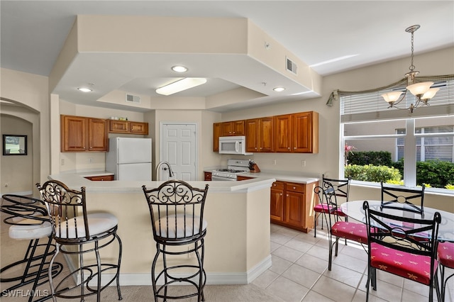 kitchen featuring brown cabinetry, white appliances, visible vents, and a breakfast bar area