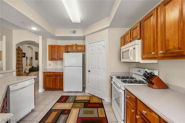 kitchen with light tile patterned flooring, white appliances, visible vents, light countertops, and brown cabinetry