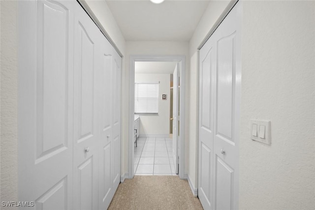 hallway with light tile patterned floors, baseboards, and light carpet