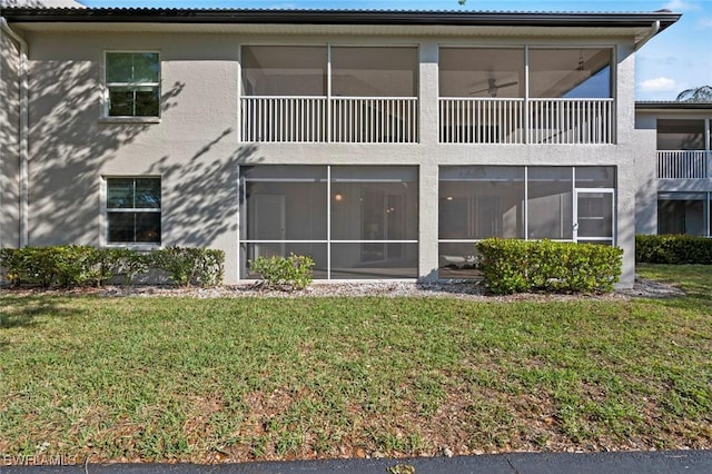 rear view of property with stucco siding, a yard, and a sunroom