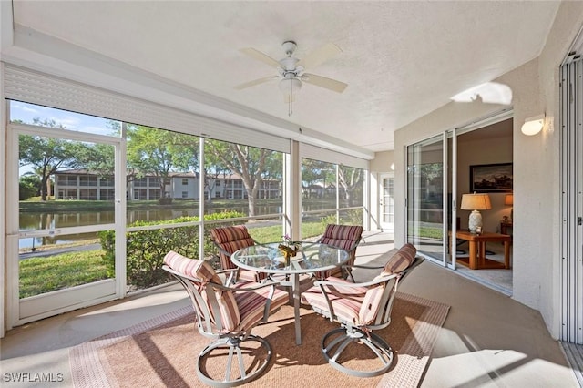 sunroom with a ceiling fan and a water view