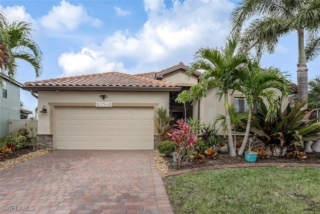 mediterranean / spanish house featuring decorative driveway, stucco siding, a garage, stone siding, and a tiled roof