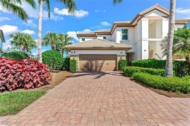 mediterranean / spanish-style house featuring a garage, a tile roof, stone siding, decorative driveway, and stucco siding