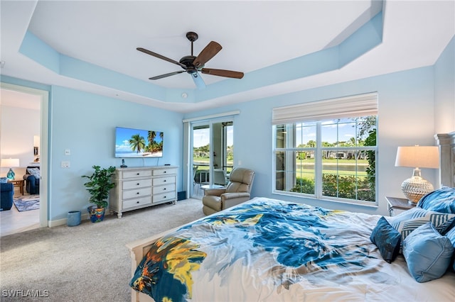 carpeted bedroom featuring access to exterior, baseboards, a tray ceiling, and a ceiling fan