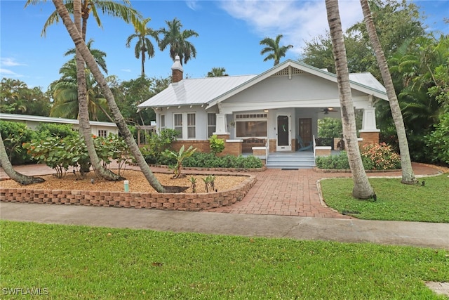 view of front of home with brick siding, a ceiling fan, a chimney, a porch, and a front yard