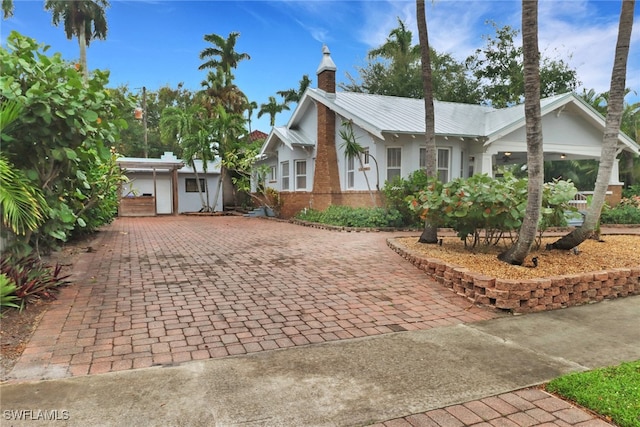 view of front facade with metal roof, decorative driveway, a chimney, and brick siding