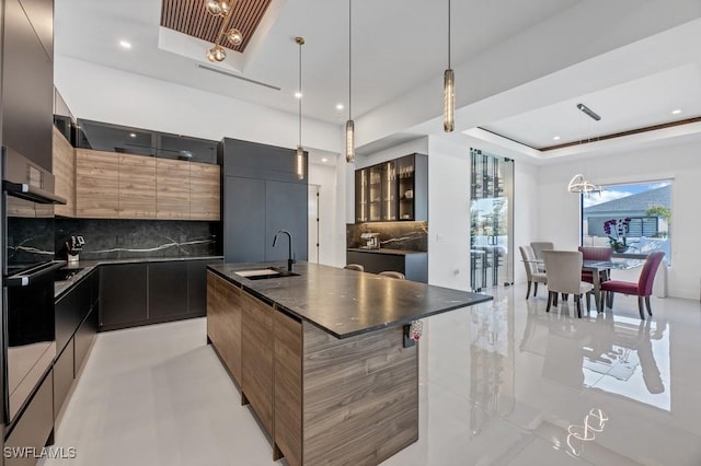 kitchen featuring a center island with sink, a raised ceiling, dark countertops, modern cabinets, and a sink