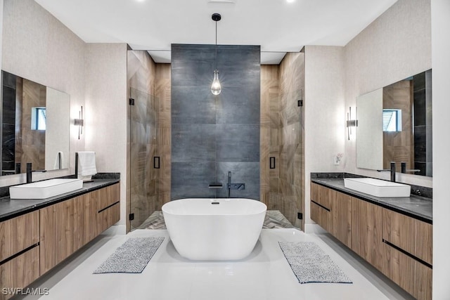 full bath featuring two vanities, a sink, a shower stall, and a freestanding bath