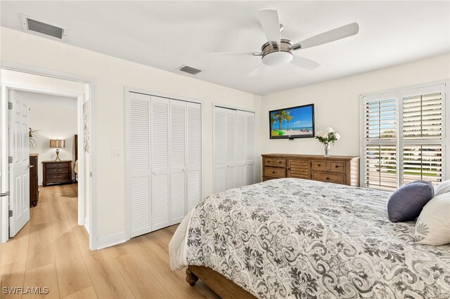 bedroom featuring light wood-style flooring, a ceiling fan, visible vents, and multiple closets