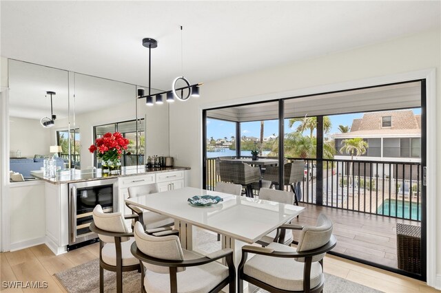 dining space featuring a water view, a notable chandelier, beverage cooler, light wood-style floors, and baseboards