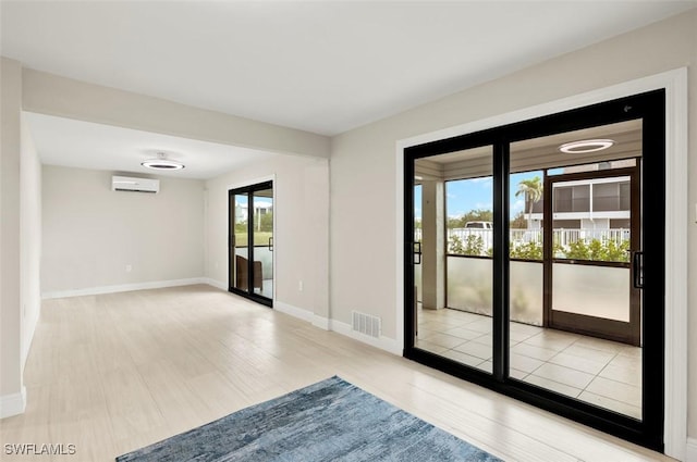 unfurnished room featuring a wall unit AC, wood finished floors, baseboards, and visible vents