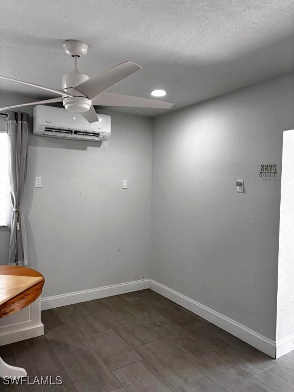 interior space with a wall unit AC, ceiling fan, baseboards, and wood finished floors