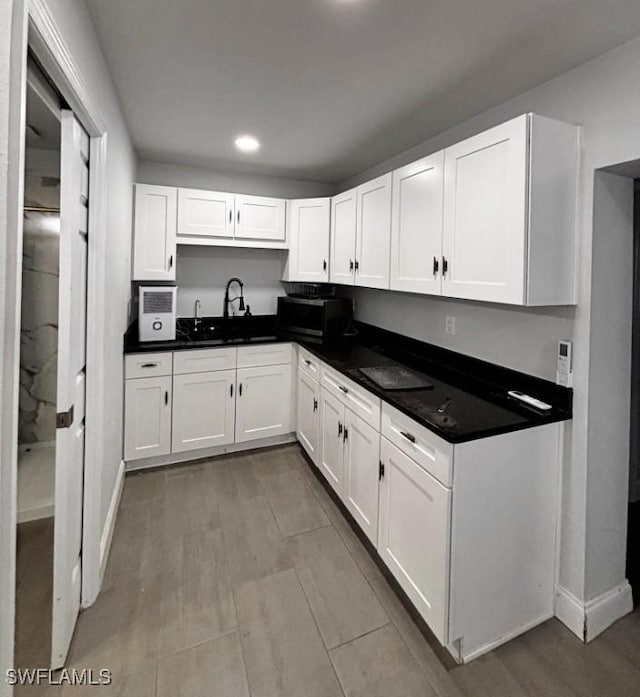 kitchen with wood finished floors, dark countertops, a sink, and white cabinetry