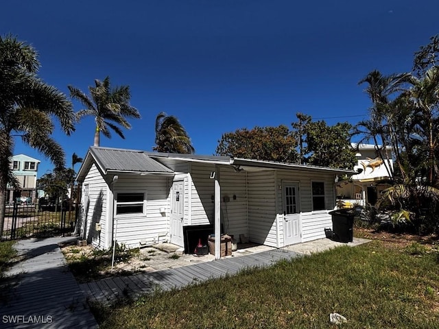 back of property featuring entry steps, metal roof, a lawn, and fence