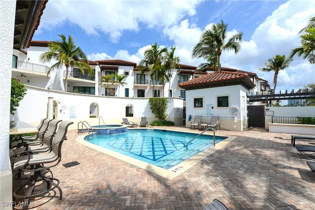 community pool with a hot tub, fence, and a patio