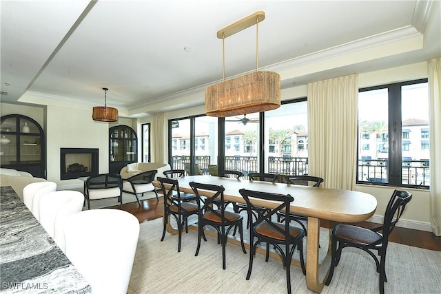 dining area with light wood finished floors, baseboards, a raised ceiling, and crown molding