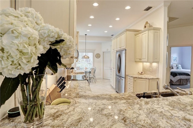 kitchen featuring visible vents, freestanding refrigerator, light stone countertops, cream cabinetry, and a sink