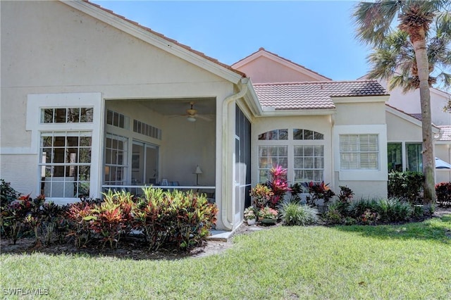 back of property featuring a tile roof, a sunroom, a ceiling fan, a yard, and stucco siding