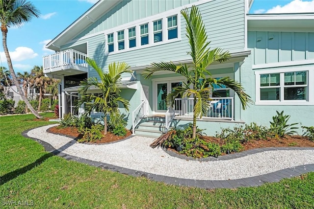 view of front of property featuring board and batten siding, covered porch, a balcony, and a front lawn