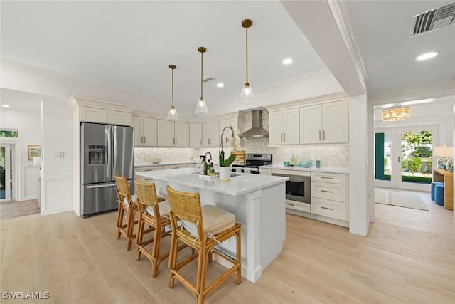 kitchen featuring stainless steel appliances, visible vents, light wood-style floors, ornamental molding, and wall chimney range hood