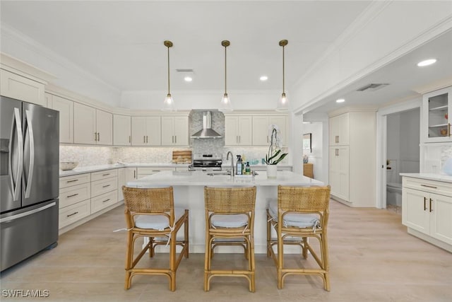 kitchen with light countertops, ornamental molding, wall chimney range hood, range, and stainless steel fridge