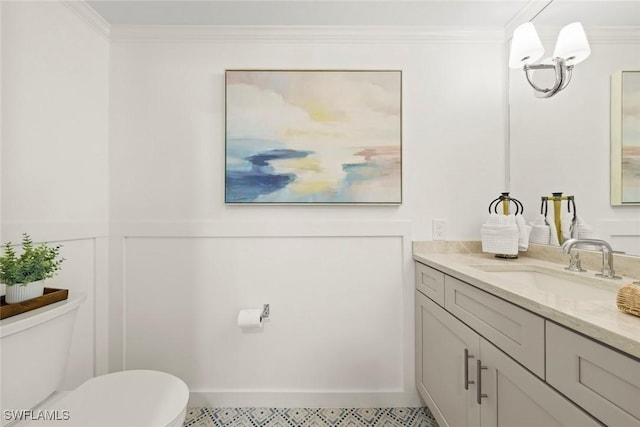 half bathroom featuring toilet, a decorative wall, a wainscoted wall, vanity, and ornamental molding