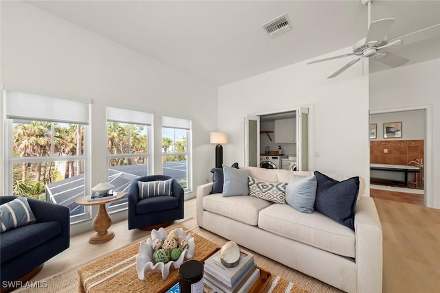 living area with washing machine and dryer, visible vents, ceiling fan, and wood finished floors