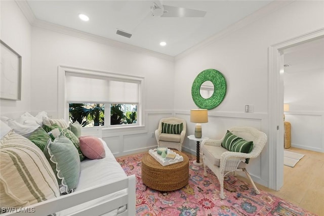 living area featuring ornamental molding, visible vents, a decorative wall, and wood finished floors