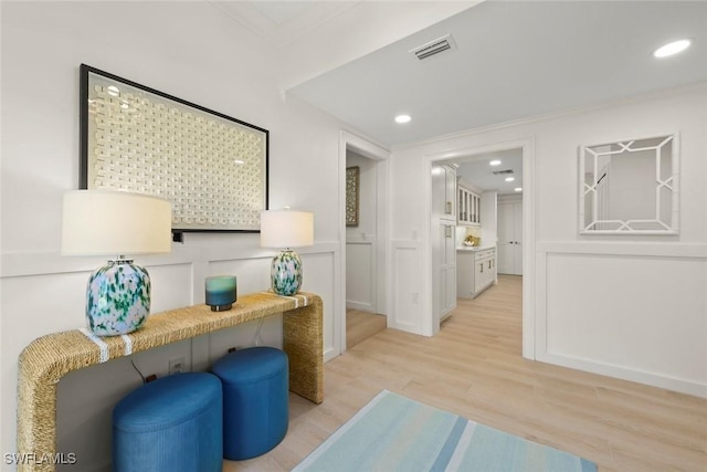 living area featuring light wood-style flooring, a decorative wall, recessed lighting, visible vents, and crown molding