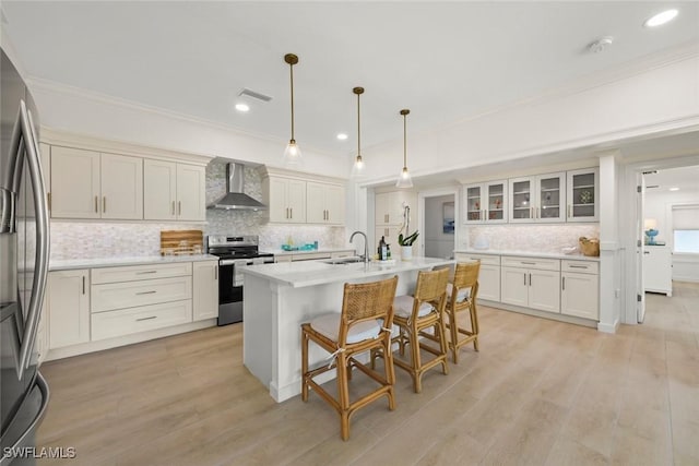 kitchen featuring light wood-style flooring, a breakfast bar area, stainless steel appliances, crown molding, and wall chimney range hood