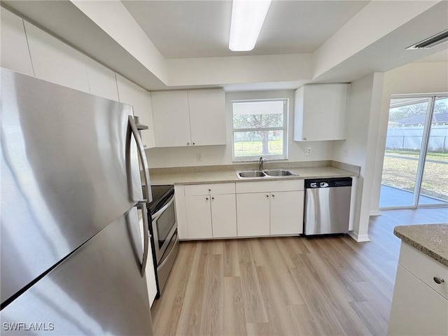 kitchen with white cabinets, appliances with stainless steel finishes, light countertops, light wood-style floors, and a sink