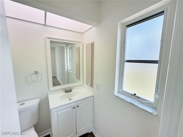 half bath with toilet, baseboards, a wealth of natural light, and vanity